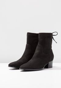 Bottines en daim noir avec bout pointu et petit talon carré. Présentent une coupe ajustée et un détail décoratif de nœud à l'arrière.