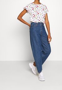 Haut à manches courtes à motif floral blanc associé à un jean large en denim bleu taille haute et des baskets blanches.