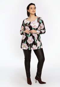 Blomstret tunika i sort velour med pink og grønne blomstermønstre, parret med tætsiddende brune læder leggings og brune højhælede sko.