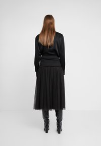 Blusa negra de manga larga con una cintura texturizada, combinada con una falda de tul negro transparente con patrones de puntos sutiles y botas de tacón hasta la rodilla.