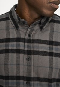 Camicia abbottonata in un motivo a quadri grigio e nero. Realizzata in un tessuto morbido, presenta un colletto a punta e bottoni neri sul davanti.