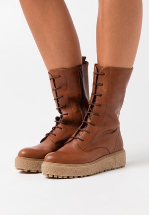 Brown leather lace-up boots with a mid-calf height, textured upper, and a chunky beige sole. Features side zipper for easy access.