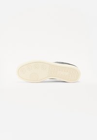 Sole of a shoe featuring a textured, rubber bottom in cream color with circular and zigzag patterns; upper portion in gray.