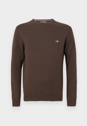 Brun stickad tröja med rund halsringning, långa ärmar, ribbade muddar och fåll. Har en liten broderad logga på bröstet.