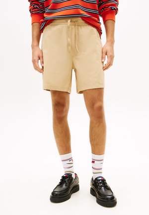 Mann iført brune shorts med snøring, stripete hvite sokker, svarte sko og en rød- og marineblåstripet langermet skjorte med oppbrettede ermer.