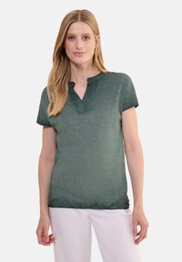 Top verde a maniche corte in morbido tessuto con una sottile texture mélange, caratterizzato da un colletto a taglio e una vestibilità comoda. Accentua un orlo curvo.