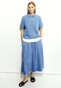 Light blue denim polo shirt with short sleeves, zipper front. Paired with a loose, matching midi skirt. Black slip-on sandals.