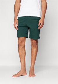 Donkergroene katoenen shorts met een relaxte pasvorm, voorzien van een elastische tailleband en een gladde textuur, gedragen met een wit T-shirt.