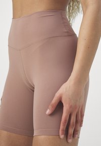 Höga shorts i ett mjukt, ljusbrunt tyg. Slät textur med minimala sömmar och en åtsittande design som når till mitten av låret.