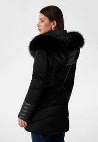 Black puffer coat with a fur-trimmed hood, featuring quilted texture and leather-accented sleeves, shown from the back.