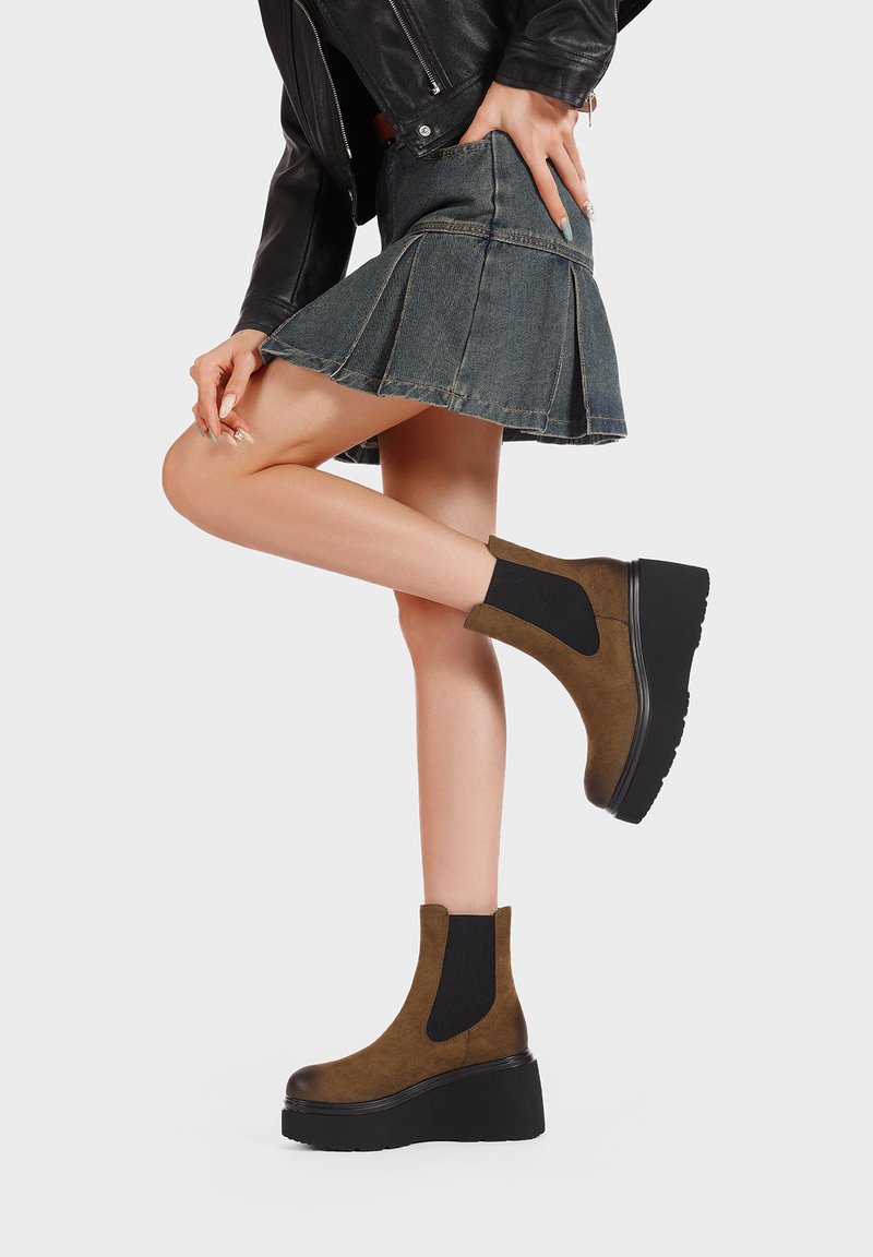 Stivali alla caviglia in suede marrone con pannelli elastici, suole a piattaforma nera chunky e punte arrotondate, indossati con una gonna di jeans e una giacca di pelle.