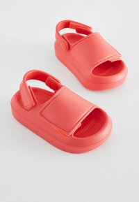 Koralfarvet børnesandaler lavet af blødt plast, med en velcro-rem, åben tå-design og tekstureret fodseng.