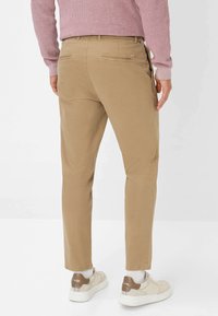 Beige katoenen chinos met een slim fit, voorzien van achterzakken en een nette zoom, gecombineerd met lichtgekleurde sneakers en witte sokken.