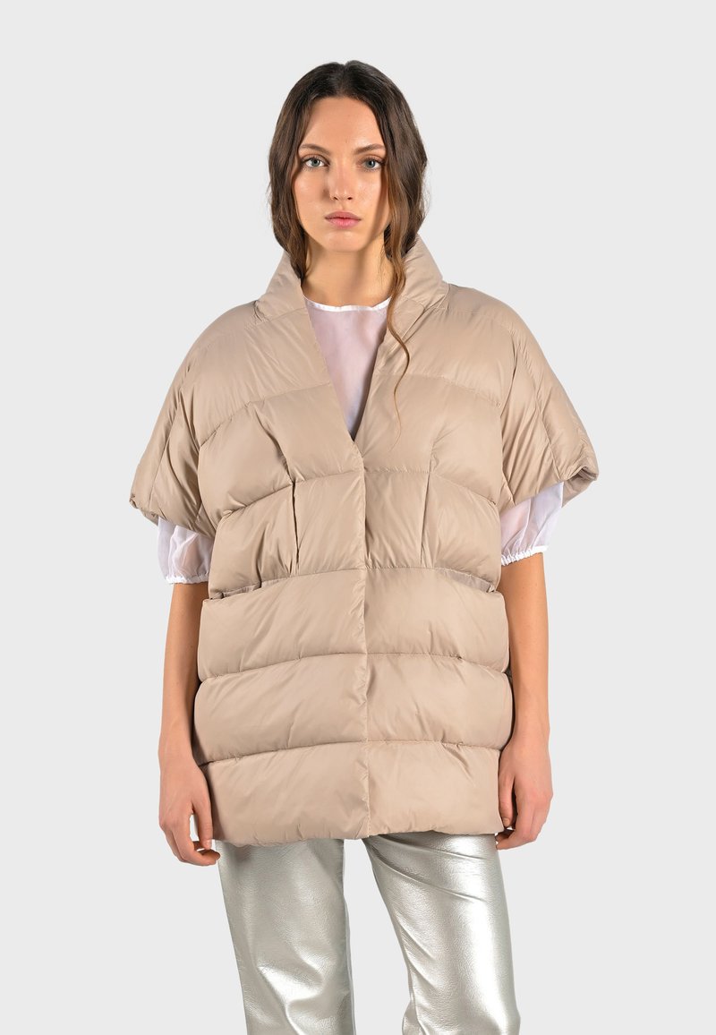 Beige puffer-väst med bred krage och korta ärmar, med quiltade sektioner och en mjuk, slät textur. Matchas med glänsande silverbyxor.