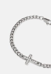 Stříbrný náramek s řetízkem, který zdobí přívěsek ve tvaru kříže osázený rhinestony, s hladkou texturou a leštěným povrchem.