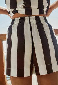 Ribede shorts med skiftende brune og hvide lodrette striber, elastisk talje, og afsluttede kanter med synlige sømdetaljer.