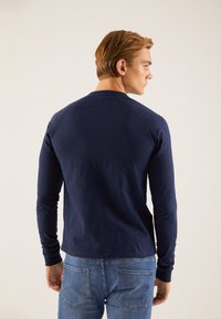 Tricou cu mânecă lungă de culoare albastru marin, confecționat din bumbac, având guler rotund și mâneci raglan, asortat cu blugi din denim albastru.