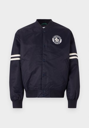 Navyblauwe bomberjack van gladde stof, met een rond logo op de linkerkant van de borst en witte strepen op de mouwen. Geribbelde manchetten.