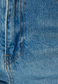 Tejido de mezclilla azul claro con una textura suave, con costuras naranjas a lo largo de las juntas y un ligero efecto de decoloración para mayor detalle.