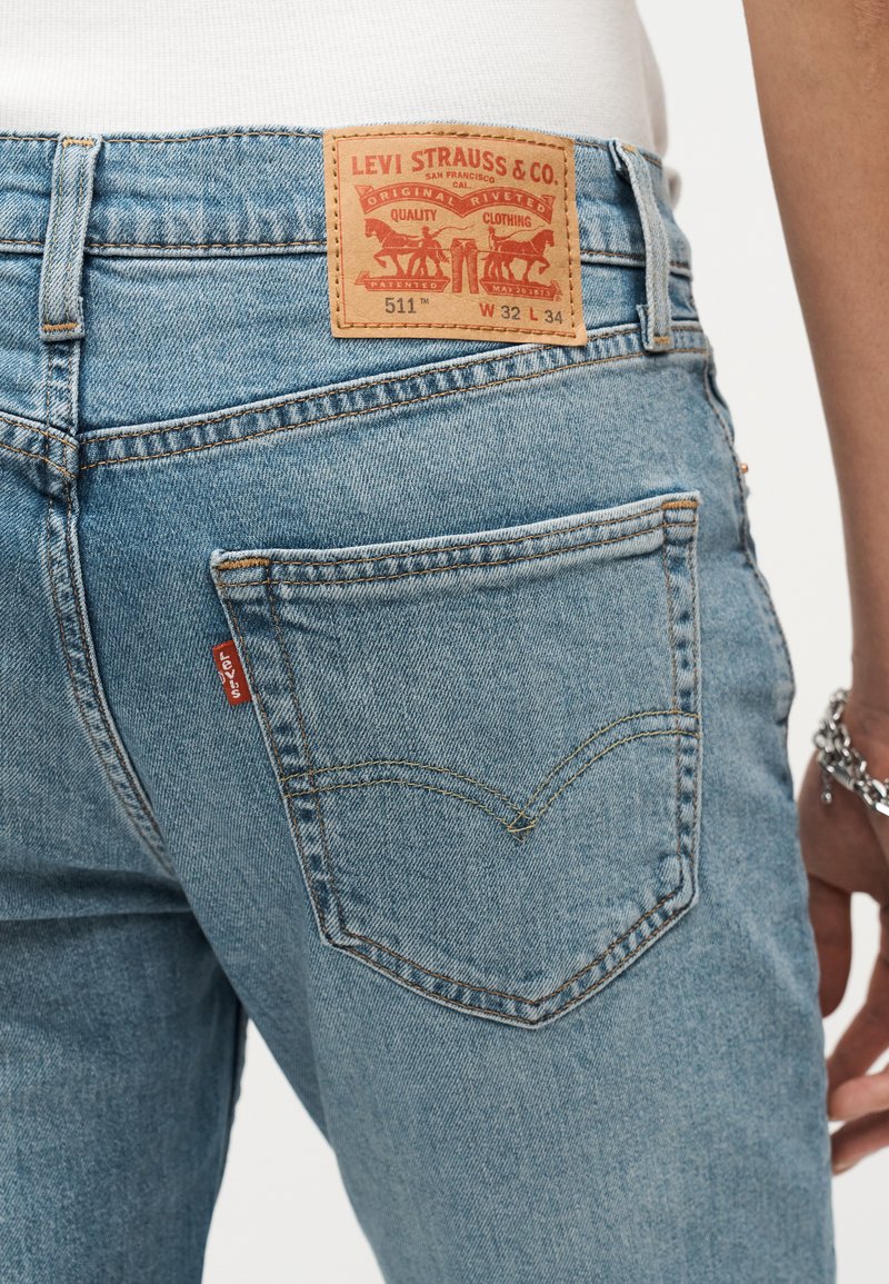 Hellblaue Levi's 511 Jeans, getragen von einer Person, zeigen die Gesäßtasche, das rote Markentag und das Leder-Brandflicken mit Größenangaben.