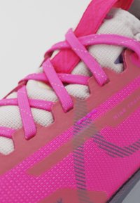Gros plan d'une chaussure d'entraînement Nike rose avec des lacets rose vif et un tissu blanc texturé en dessous.