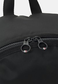 Zaino in nylon nero con texture liscia, dotato di chiusura con zip e doppi tiranti neri, con dettagli colorati sulla zip.