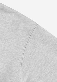 Zbliżenie na jasnoszary materiał, ukazujące teksturę oraz detale szwu na rękawie odzieży, sugerujące casualowy styl ubioru.