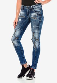 Blaue enge Skinny-Jeans mit einer körperbetonten Passform, die dekorative Reißverschlüsse und distressed Details an den Beinen für zusätzlichen Textur aufweisen.