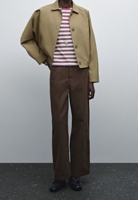 Pantaloni larghi marroni, camicia a righe a maniche corte con rosso, blu e bianco, giacca beige cropped con bottoni e scarpe nere con lacci.