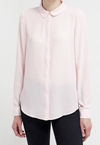 Blouse rose clair à manches longues avec un devant boutonné et un col arrondi ; tissu lisse et texturé, ourlet arrondi.