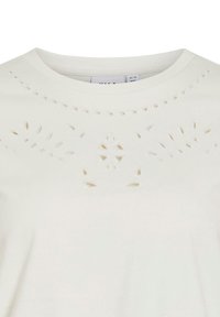 Camiseta blanca de algodón con patrones recortados decorativos y cuello redondo. La tela tiene una textura suave y un corte holgado.