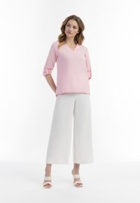 Lys pink, kortærmet bluse med V-udskæring og op rullede ærmer, parret med brede hvide bukser og lyse hæle sandaler.