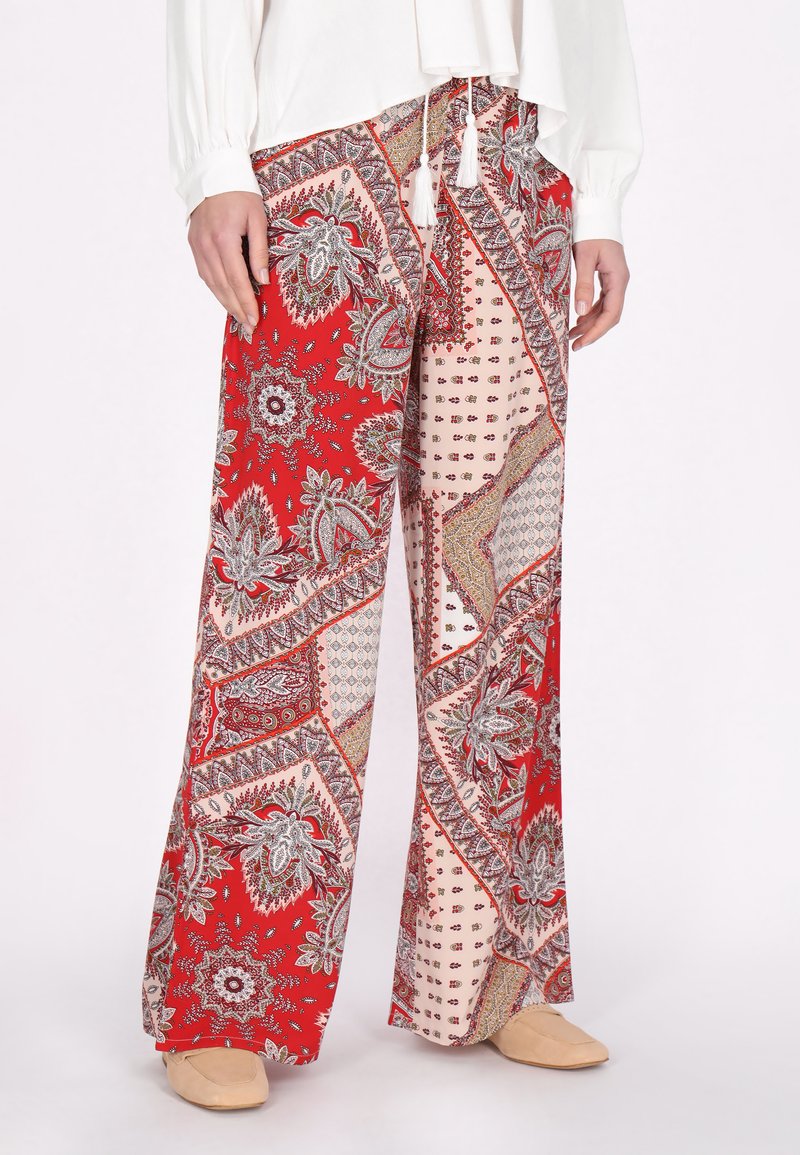 Pantaloni a gamba larga con un motivo paisley rosso, caratterizzati da sezioni pastello a contrasto, con cuciture decorative e nappine legate in vita.