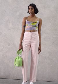 Jeans de cintura alta em rosa pastel, combinados com uma blusa curta roxa de padrão floral e uma pequena bolsa verde. Ténis brancos completam o visual.