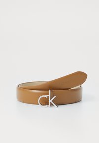 Ceinture en cuir tan avec une boucle en argent poli en forme de "CK" et une texture lisse. Le design est simple et épuré avec des accents minimaux.