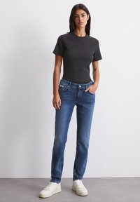 Svart ribbet t-skjorte med korte ermer, kombinert med blå slim-fit jeans og hvite joggesko. Enkel design med en tettsittende silhuett.
