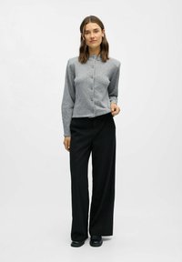 Grijze wollen cardigan met knoopsluiting, ronde hals en lange mouwen; gecombineerd met zwarte pinstripe wijde broek en zwarte schoenen.