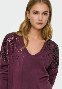 V-Ausschnitt Pullover in Dunkelpurpur mit Paillettenverzierung auf den Schultern. Weiches Strickmaterial mit lockerer Passform und langen Ärmeln.