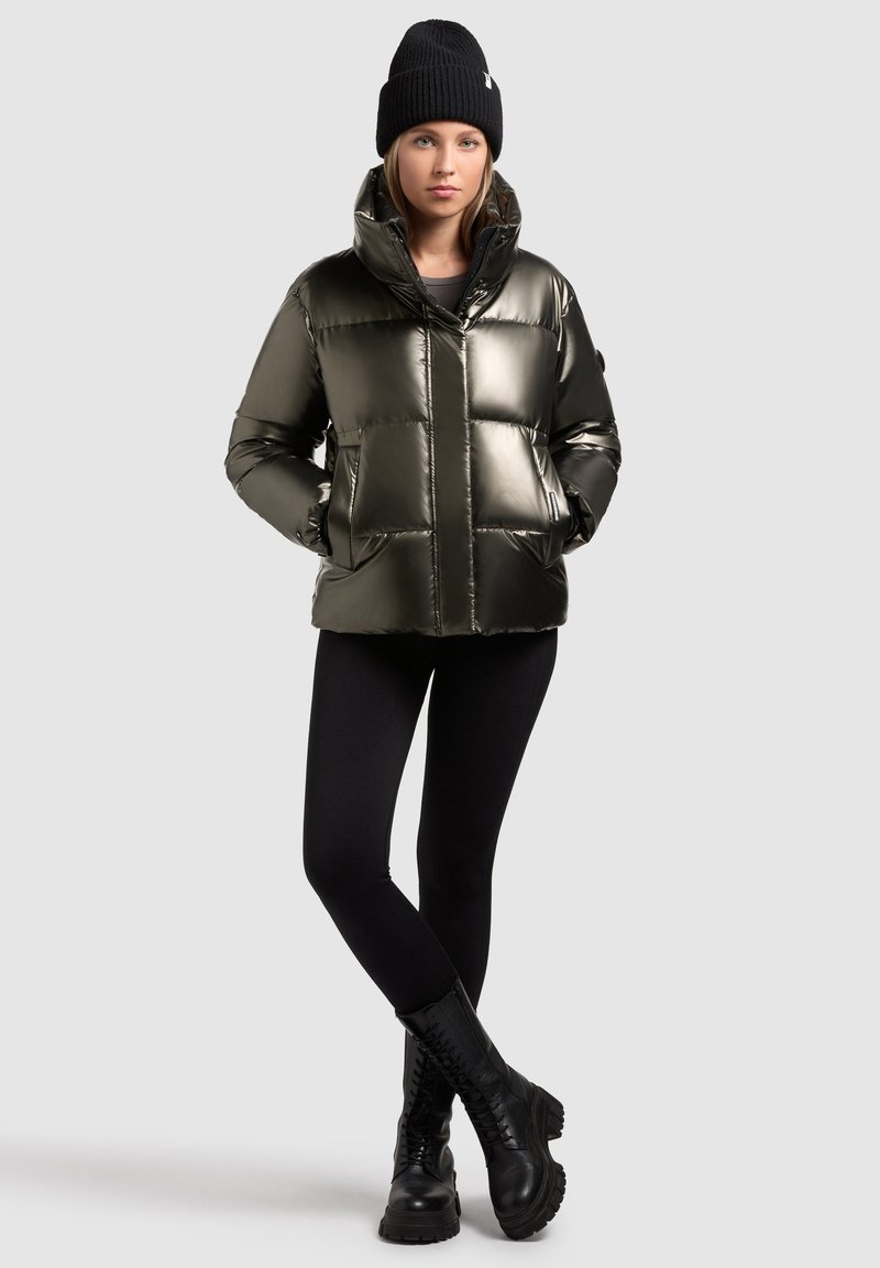 Olivenfarvet pufferjakke med et skinnende, quiltet design, høj krave og lynlås, parret med sorte leggings og snørebåndede kampstøvler.