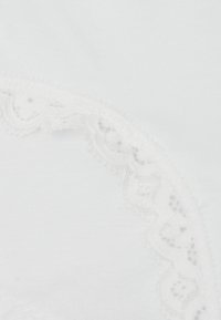 Witte katoenen kledingstukken met ingewikkelde kantafwerking langs de rand, met een delicate geschulpte patroon en een zachte textuur.