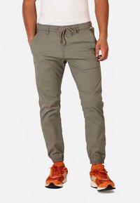 Pantalones cargo de color verde claro con cinturilla elástica, cierre de cordón, bolsillos laterales y corte ajustado. Llevados con zapatillas deportivas naranjas.