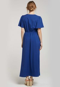 Robe maxi bleue avec des manches courtes flottantes, taille élastique et coupe fluide. Tissu lisse d'une couleur unie et design jusqu'aux chevilles.