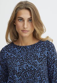 Top in stampa leopardo blu e nera con scollatura rotonda, maniche corte e tessuto morbido e strutturato. Design semplice e moderno con un motivo audace.