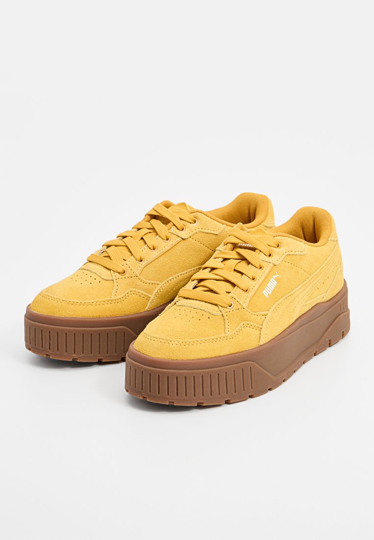 Zapatillas de color mostaza con acabado de ante, que presentan una suela de goma marrón gruesa, cordones redondos y detalles del logo en el lateral.