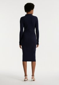 Marineblaues geripptes Strickkleid mit langen Ärmeln, hohem Kragen und Midi-Länge, das eine enganliegende Silhouette und eine subtile Textur aufweist.