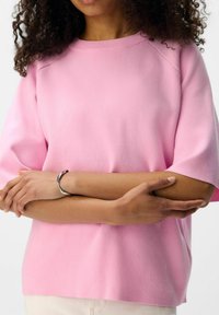 Rosa bomuldsbluse med korte ærmer, ribbet rund halsudskæring og afslappet pasform. Glat tekstur med synlige sømme langs skuldrene.