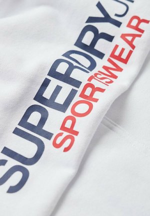 Tessuto bianco con la scritta "SUPERDRY SPORT SWEAR" stampata in grandi lettere blu navy e rosse.