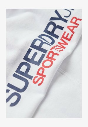 Tessuto bianco con la scritta "SUPERDRY SPORT SWEAR" stampata in grandi lettere blu navy e rosse.