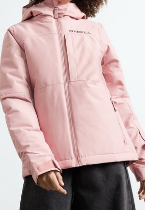 Personne portant une veste zippée rose clair O'Neill avec capuche et sangles velcro aux poignets, associée à un pantalon foncé, sur un fond uni.