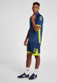 Mørkeblå atletisk sæt med limegrønne accenter; polo med korte ærmer, matchende shorts med logo detaljer og mørke sneakers.